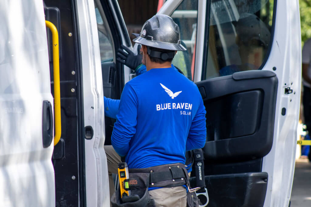 Blue Raven Solar installer talking to coworker at door of install van in proper equipment and BRS branded t-shirt
