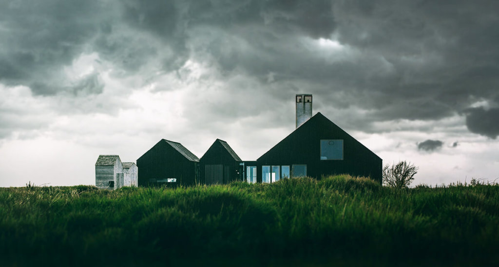 Minmal black house surrounded by tall green grass and dark rain clouds in the background