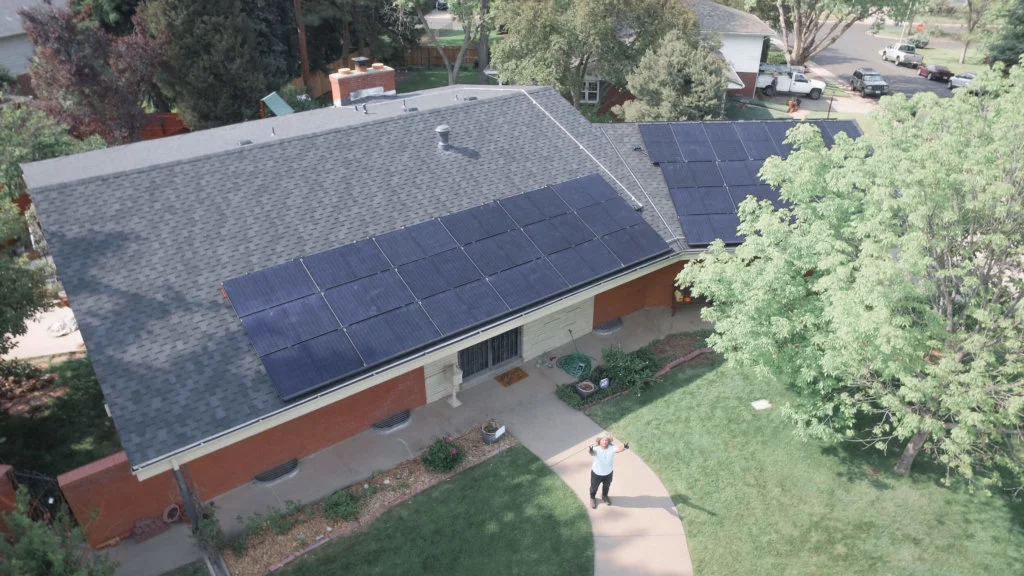 Large solar panel installation with customer standing on sidewalk, in front of house