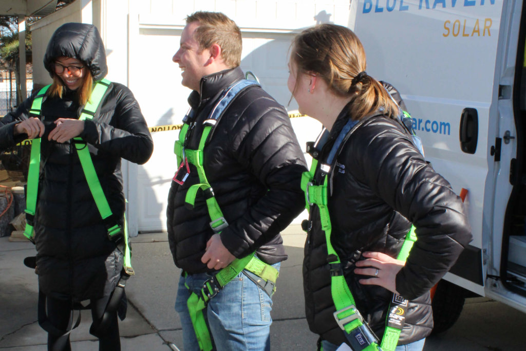 Three Blue Raven Solar employees in bright green harnesses and black puffer coats, in preparation for getting on the roof