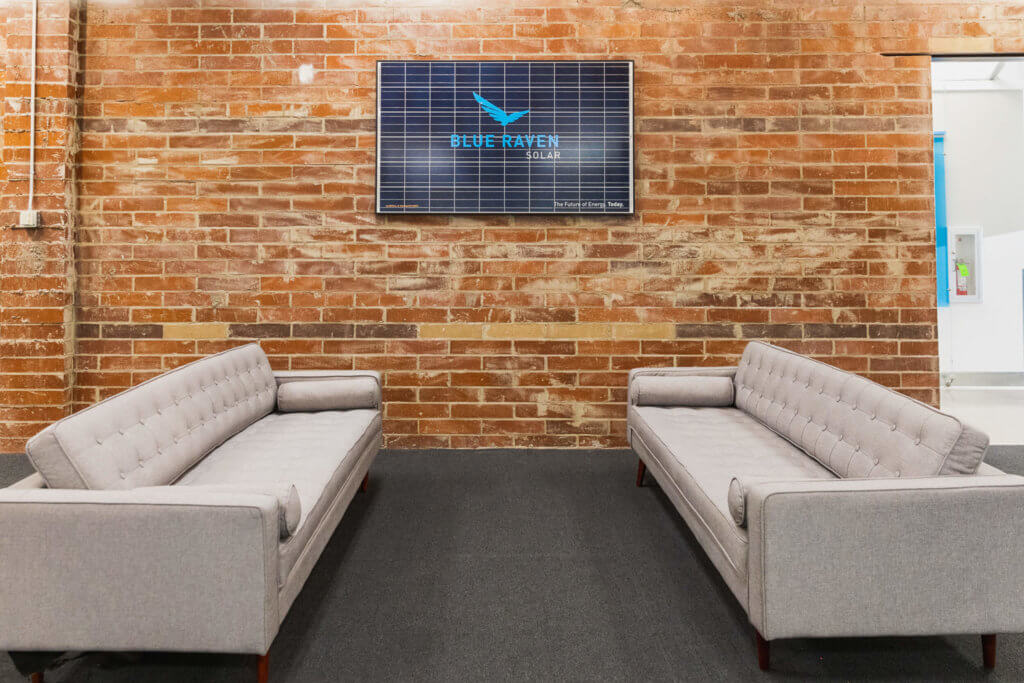 Blue Raven Solar corporate office featuring two grey couches in front of an exposed brick wall and the logo mounted on a solar panel