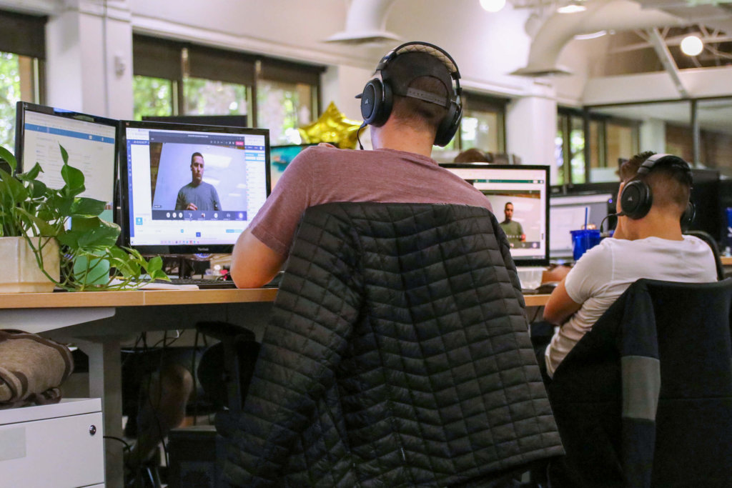 Two male employees with headphones, watching training videos in an office setting