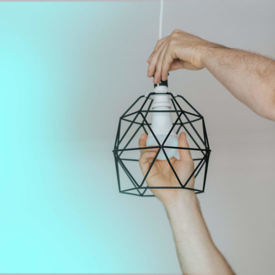 Human hands screwing in a light bulb into a modern ligh fixture with a turquoise and grey background