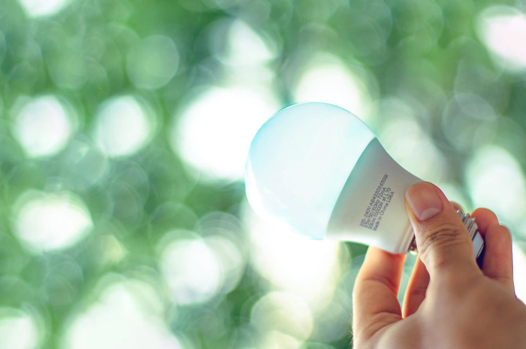Light bulb grasped in hand against an unfocused and green background