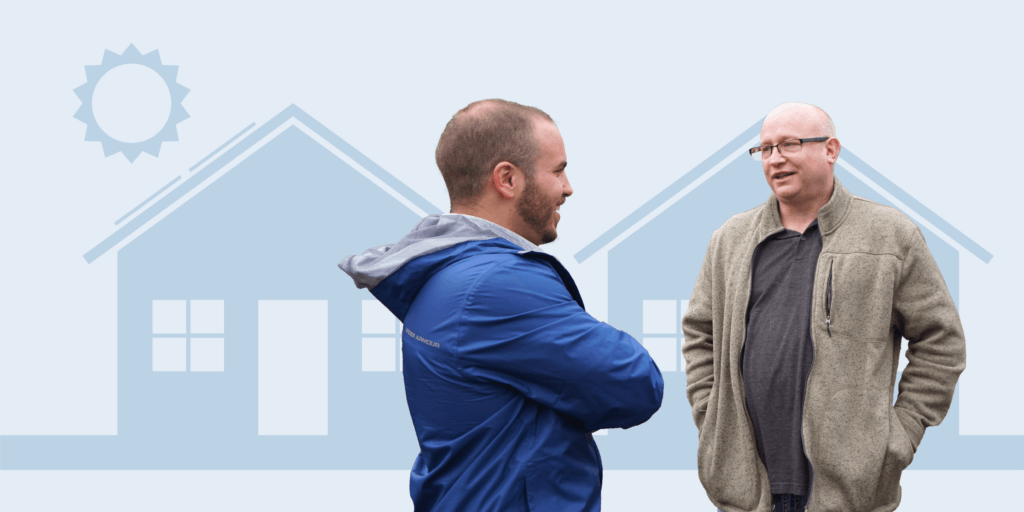 Two males standing and talking in front of two house graphics