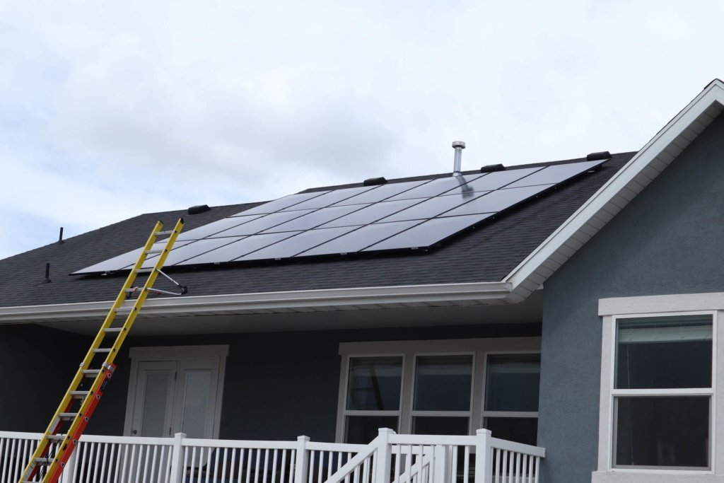 18-panel solar system installed on blue exterior house with yellow ladder leading up to it