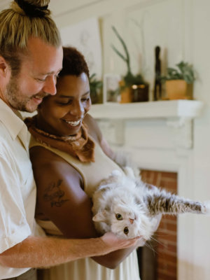 White male next to black woman holding a white and grey cat