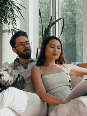 A male and female, sitting on the couch together with their dog