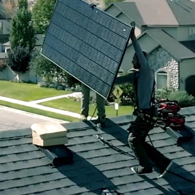 Two solar installers, carrying solar panel on roof to get into position