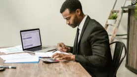 Black male in a suit, sitting at a desk filing tax documents and other paperwork