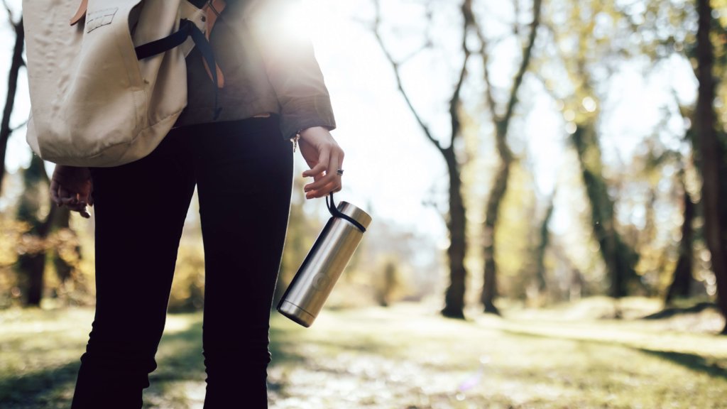 Woman facing the sun with a backpack, holding a reusable water bottle