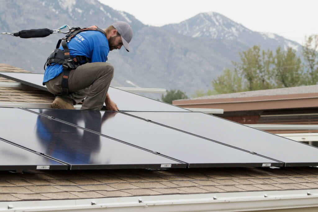 Solar installer in Orem, Utah aligning panels on roof while being harnessed for safety measures
