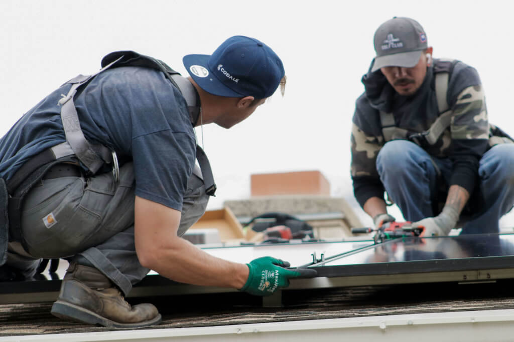 Two Blue Raven Solar installers on roof, aligning solar panels during an install