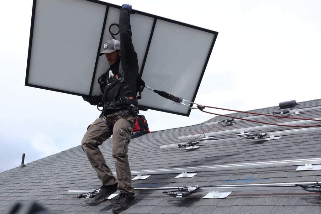 One solar installer on roof, carrying solar panel to put into place in Spanish Fork, Utah