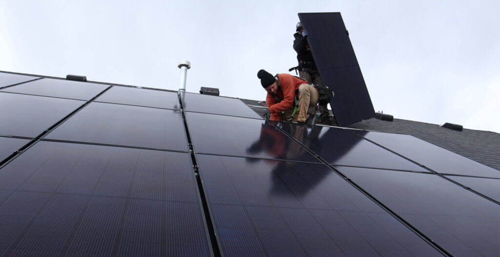 A couple of solar panel installers, on roof, positioning panels in a grid format and securing