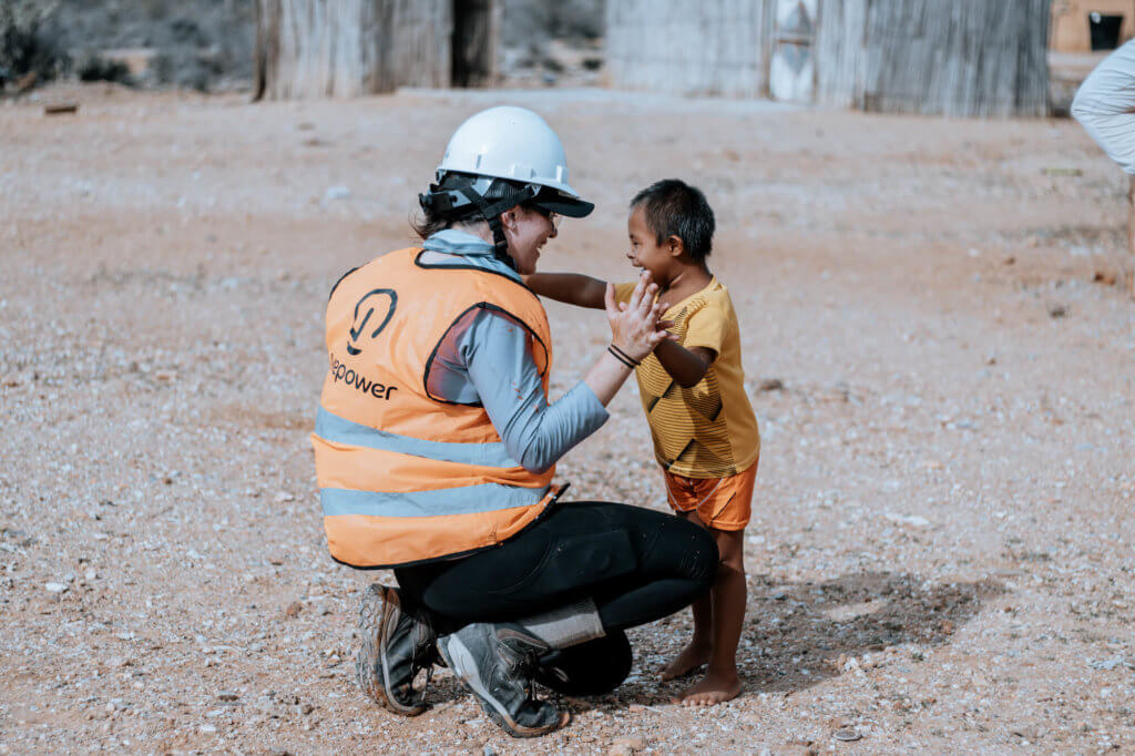 GivePower in an orange vest with white hardhat, swatting down and holding hands with a small, young boy