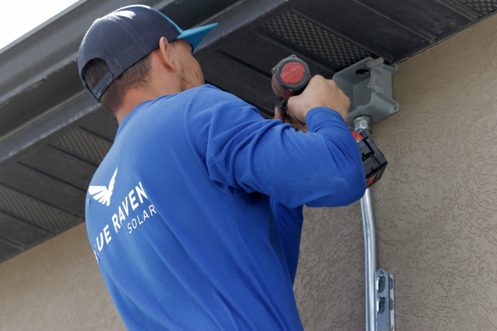 Blue Raven Solar installer working on electrical and installing conduit with drill