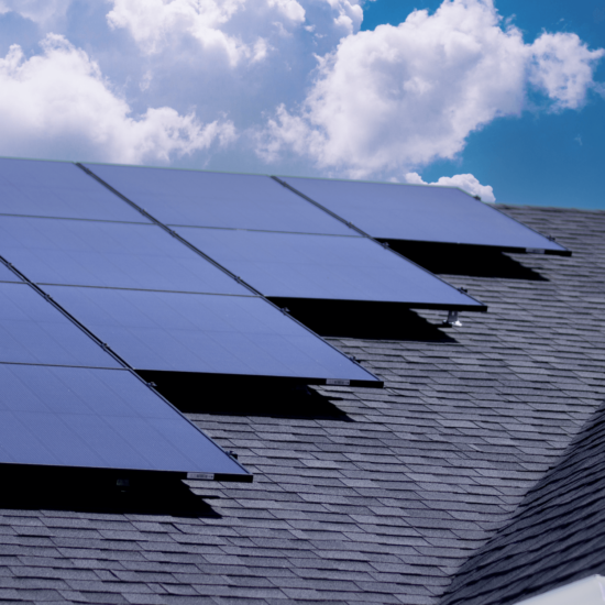 Multiple monocrystalline solar panels installed on a roof with bright clouds in the background