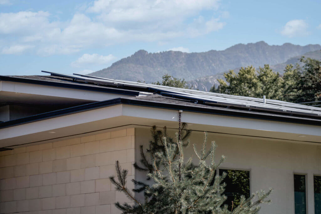 Up close view of roof line, featuring custom solar panel installation and mountains and blue sky in background