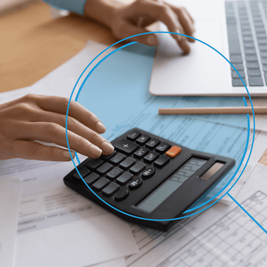 Individual working on a black calculator, sitting on top of paperwork, and laptop