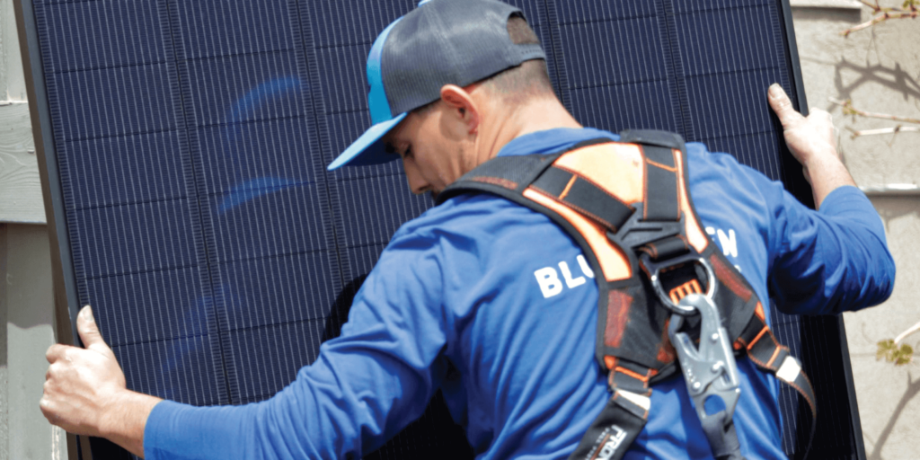 Blue Raven Solar installer in a harness, holding a solar panel