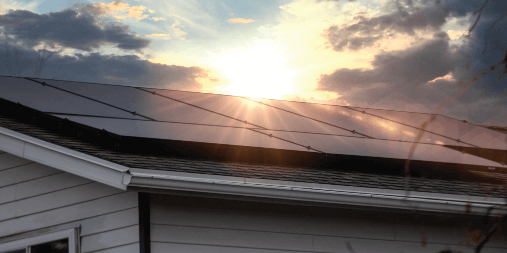 How Does a Home Solar System Work-01 Solar panel system installed on roof with the sun shining brightly through darker clouds
