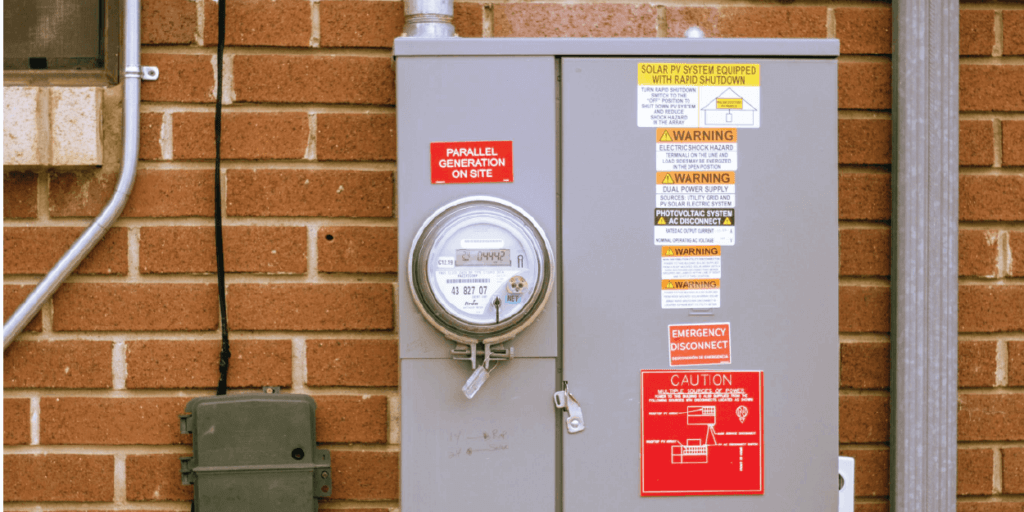 Electrical panel connected to red brick house featuring multiple caution stickers and other disclaimers