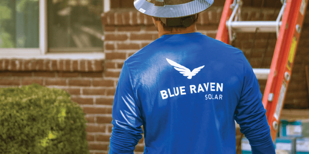 Blue Raven Solar installer in a blue branded shirt and hard hat approaching an orange ladder