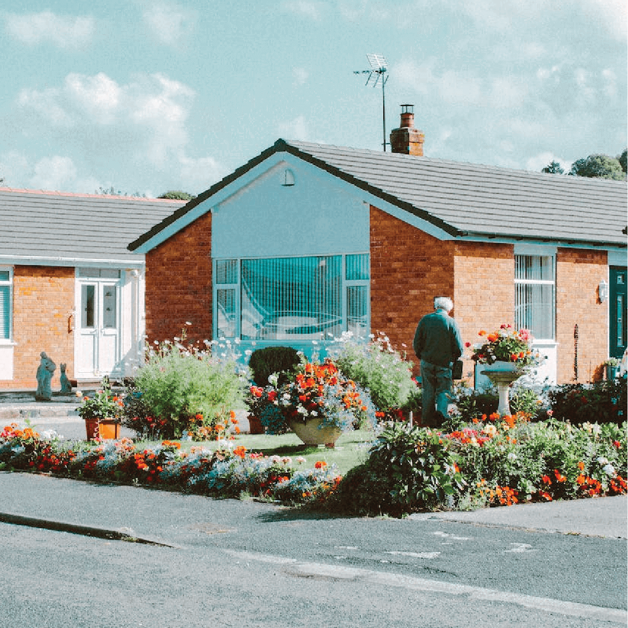 Male watering flowers outside of an orange, red brick, free-standing, single-level home