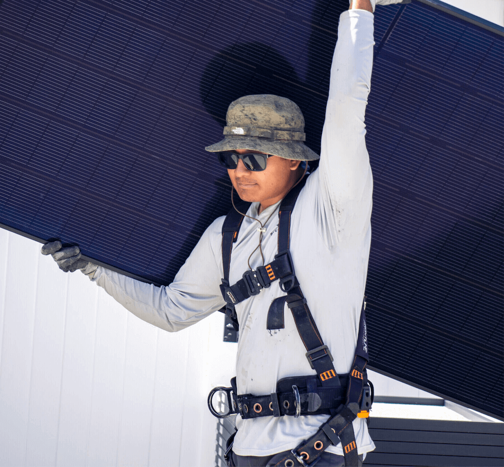 Male, Blue Raven Solar installer holding a PV panel above his head in preparation for placement on the roof