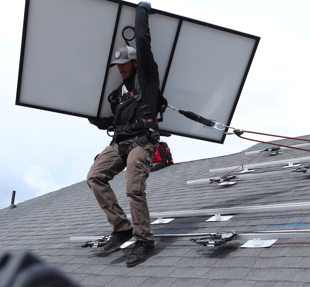 Male, Blue Raven Solar installer holding a PV panel above his head-on a roof during an installation