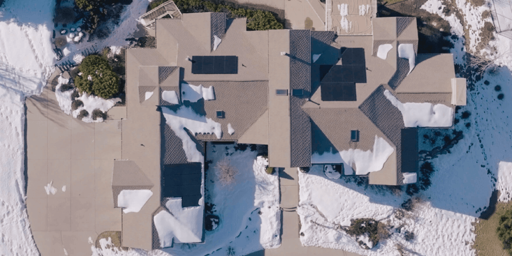 Does Solar Work in Snow-02 Aerial view of a large house with multiple PV panels installed and snow intermixed
