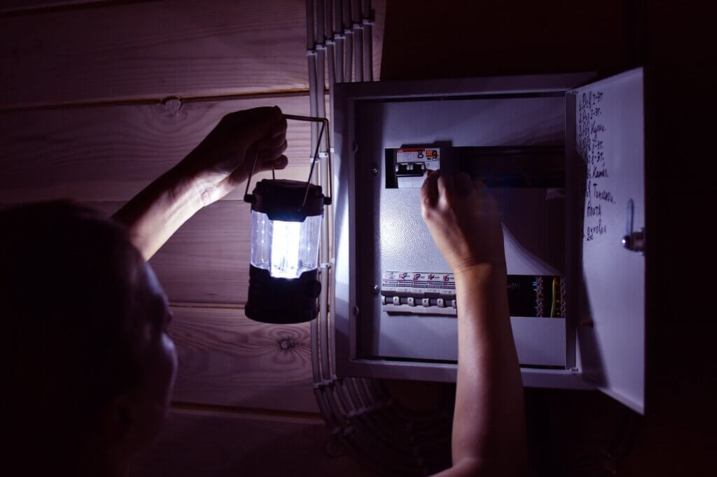 Individual holding a lamp, inspecting their electrical box in the dark