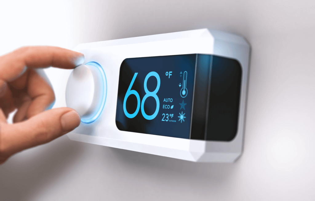 Smart thermostat featuring 68 degrees installed on white wall and a hand adjusting the knob