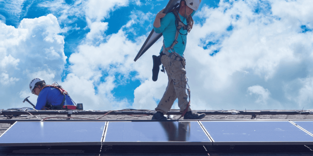 Blue Raven Solar installer carrying a solar panel on his back, on a roof, during an installation
