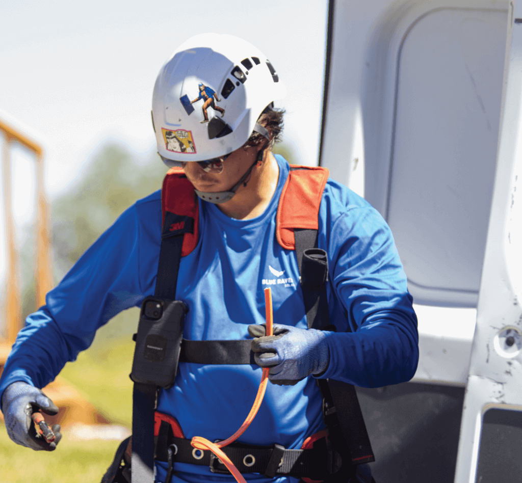 Blue Raven Solar installer in a harness and hard hat, retrieving specialized tools from the branded van