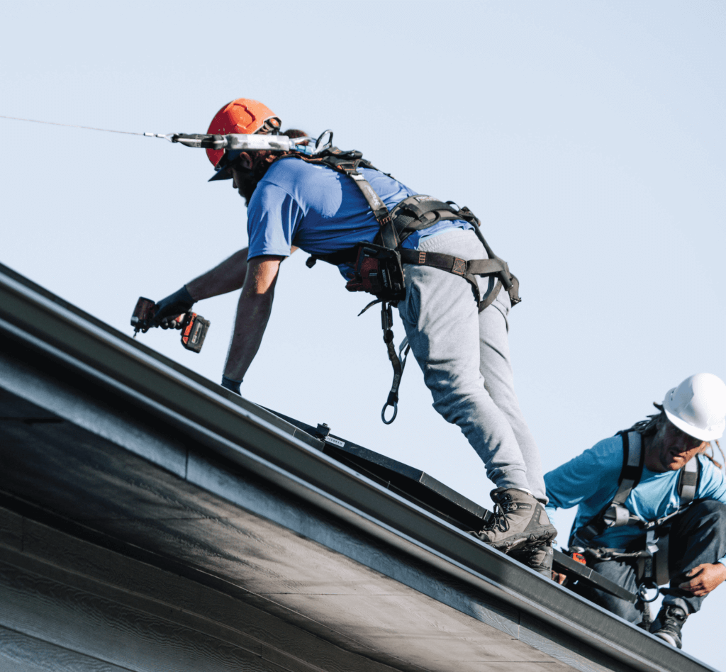 Two Blue Raven Solar installers, in safety equipment, securing solar panels to roof