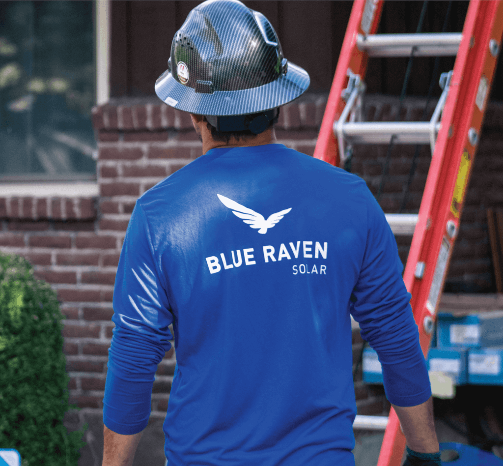 Blue Raven Solar installer in a branded blue, long-sleeve shirt with a hard hat approaching a ladder