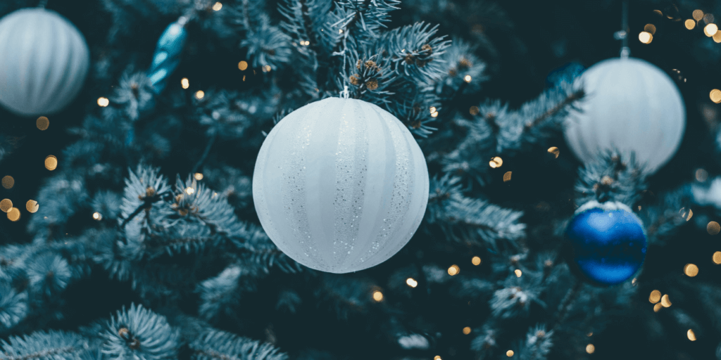 White and royal blue round holiday ornaments on a faux tree with golden lights in the background