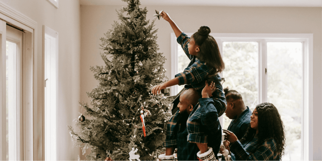 A family wearing matching holiday pajamas decorates a Christmas tree