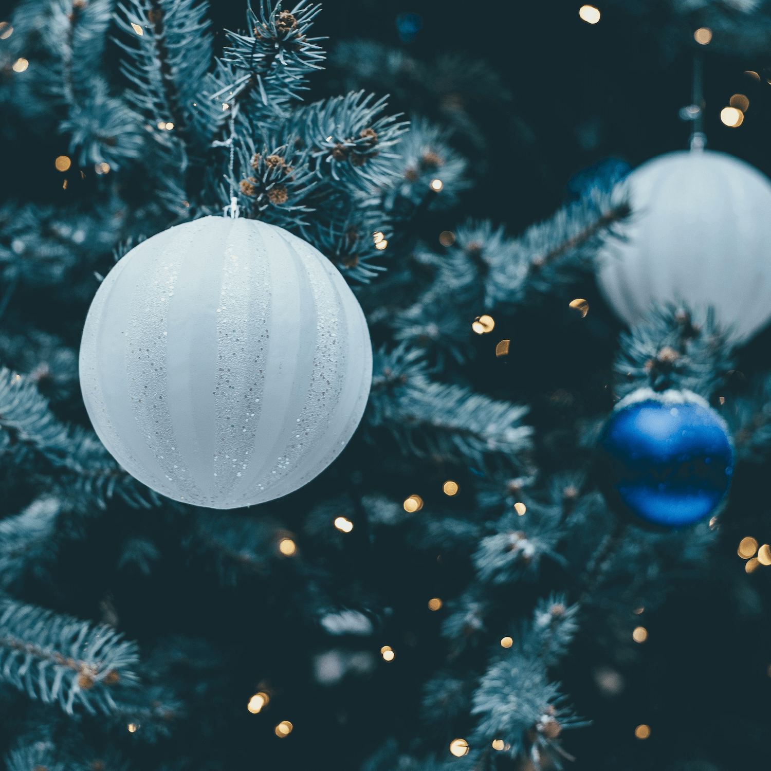 White and royal blue round holiday ornaments on a faux tree with golden lights in the background